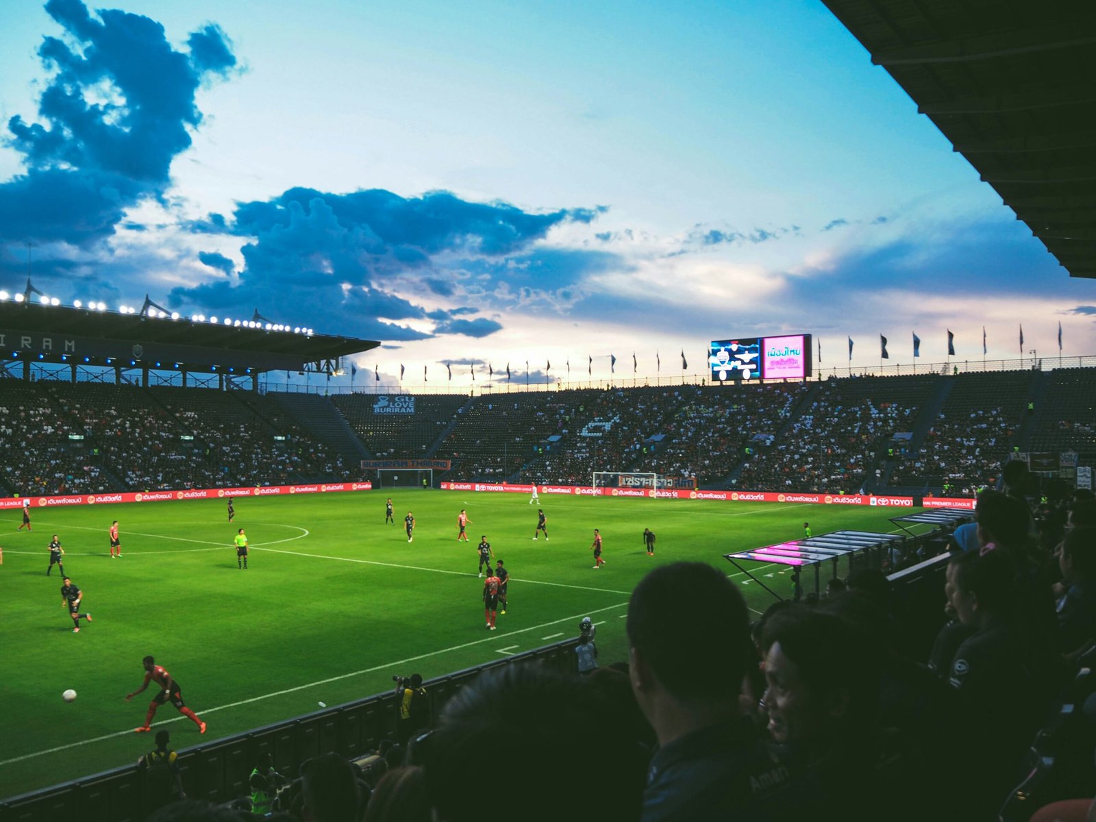 Sunset football stadium with players in action and fans filling the stands during a live match.